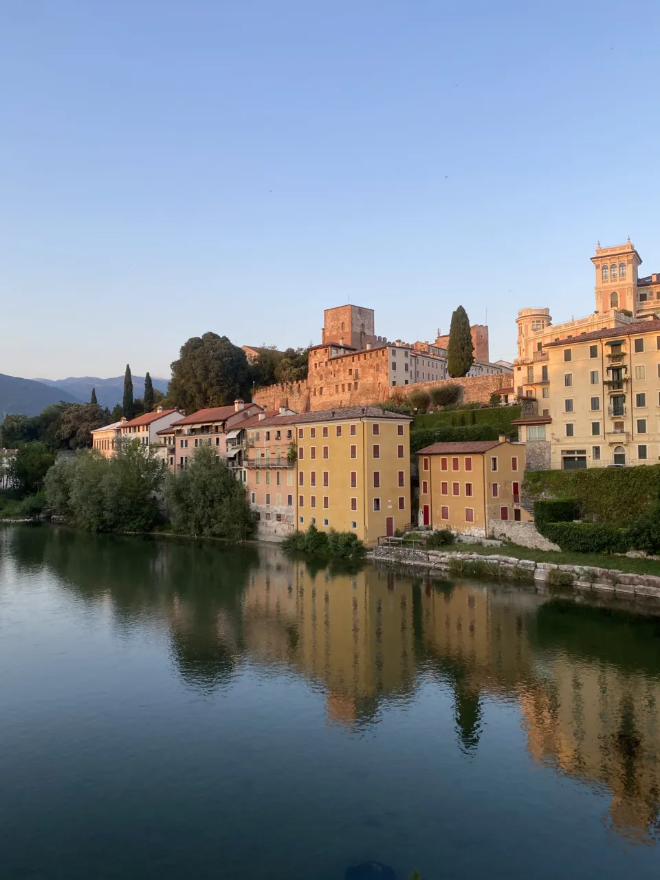 Riverside houses of Bassano del Grappa reflected in the Brenta at golden hour