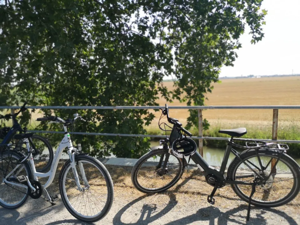 Two e-bikes parked on a railing by a canal and wheat fields