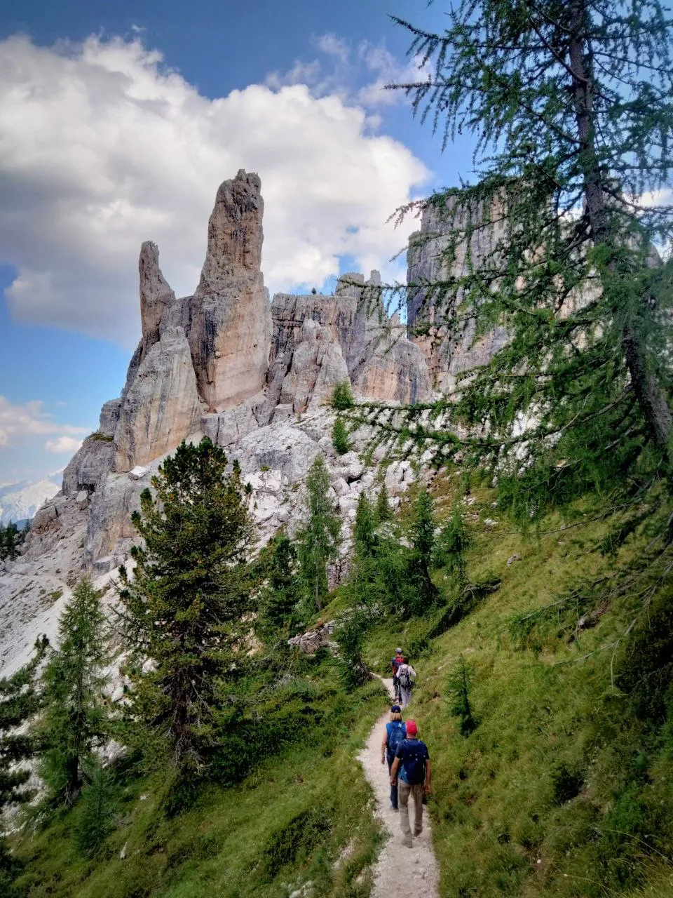 Hikers on a larch-lined trail beneath slender limestone pinnacles