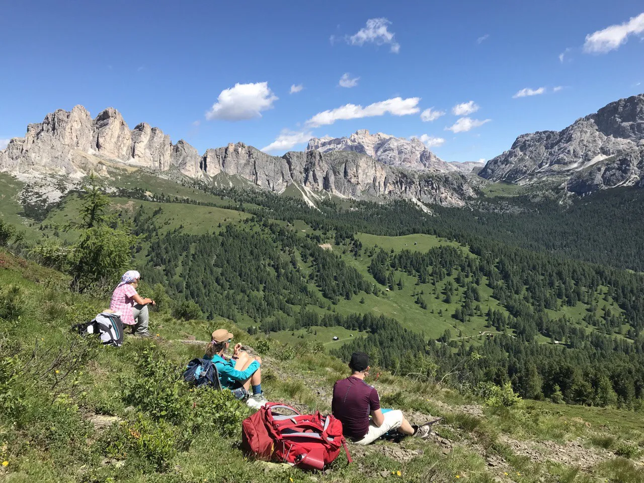Hikers resting on an alpine meadow facing a long Dolomite ridge